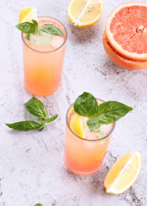 Zwei Grapefruit-Limonaden mit Zitrone, Basilikum und Eiswürfeln auf hellem Hintergrund