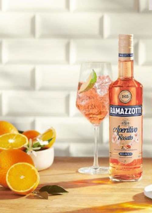 Ramazzotti Aperitivo Rosato mit Eis im Weinglas neben frischen Orangen