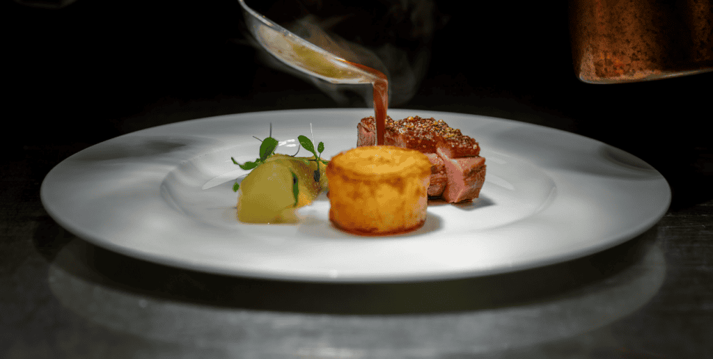 Fein angerichtetes Gourmetgericht mit rosa gebratenem Fleisch, Kartoffelbeilage und Sauce