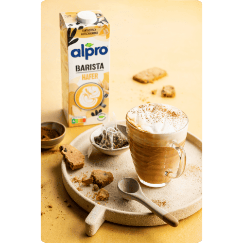 Cappuccino mit Milchschaum und Alpro Barista Haferdrink auf einem Tablett mit Keksen