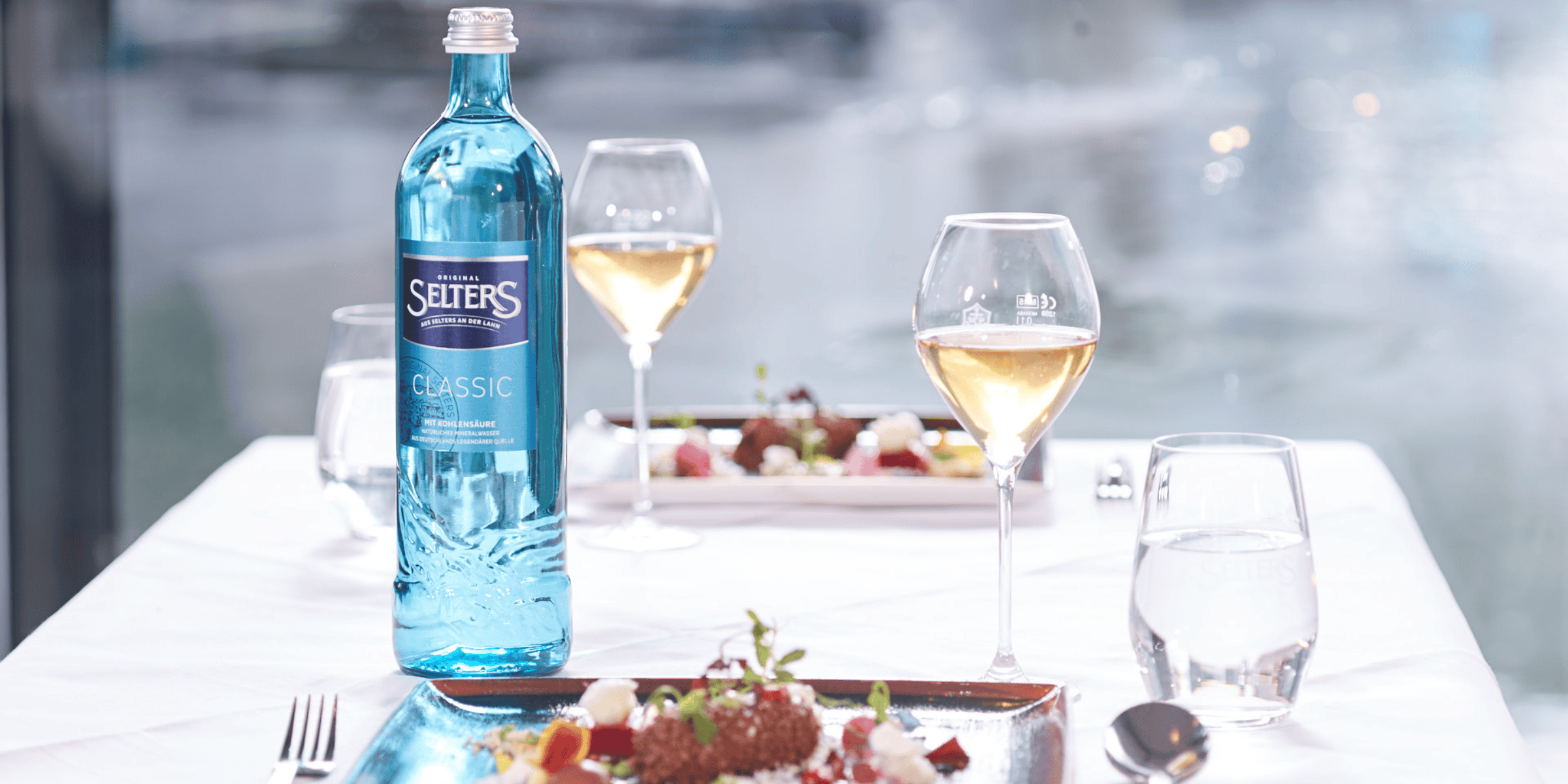 Selters Classic Mineralwasserflasche auf gedecktem Tisch mit Wein und Speisen