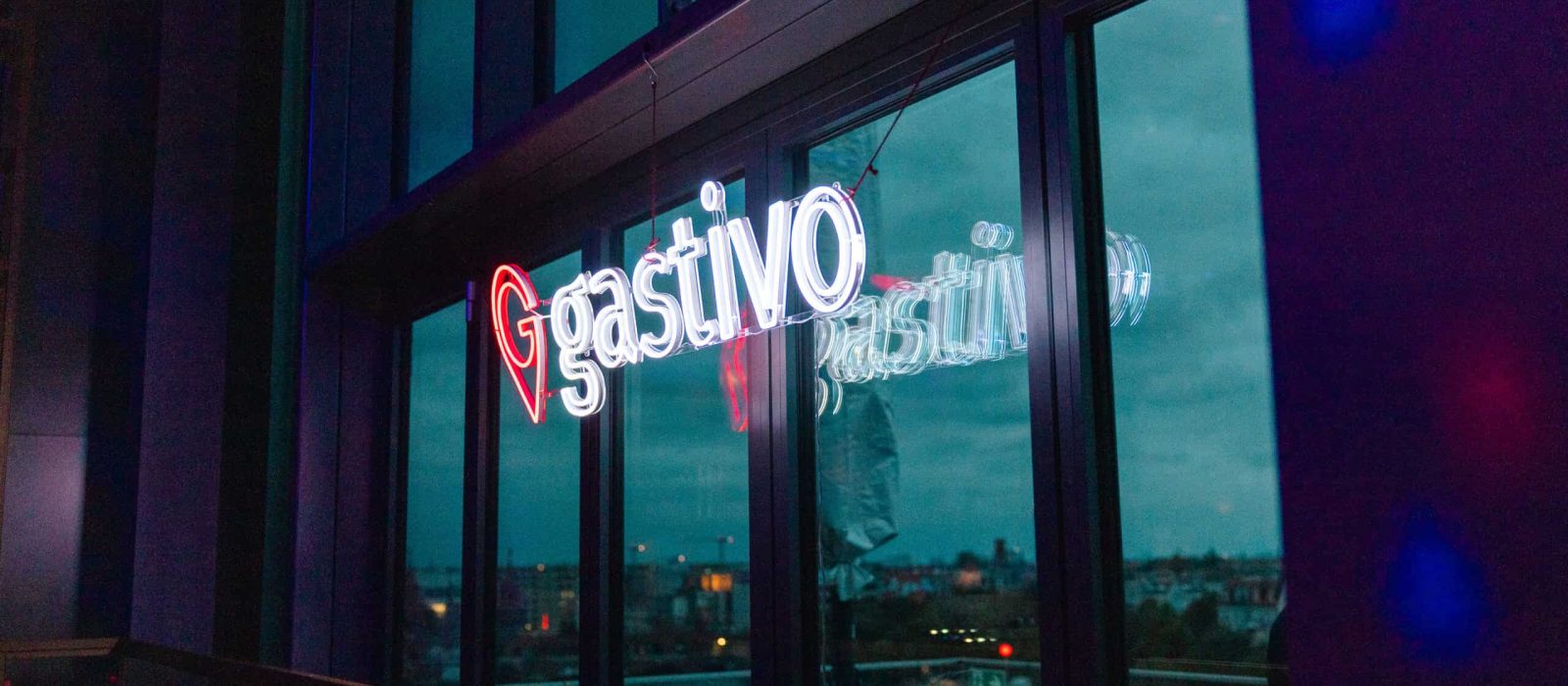 Gastivo Neon-Schriftzug an großer Glasfassade bei Abendveranstaltung mit Blick über die Stadt