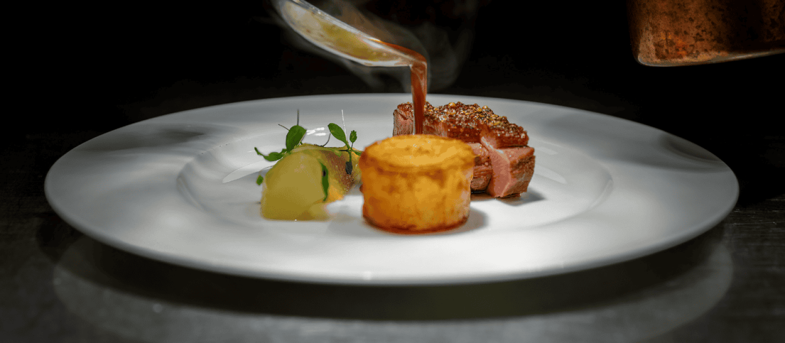 Fein angerichtetes Gourmetgericht mit rosa gebratenem Fleisch, Kartoffelbeilage und Sauce