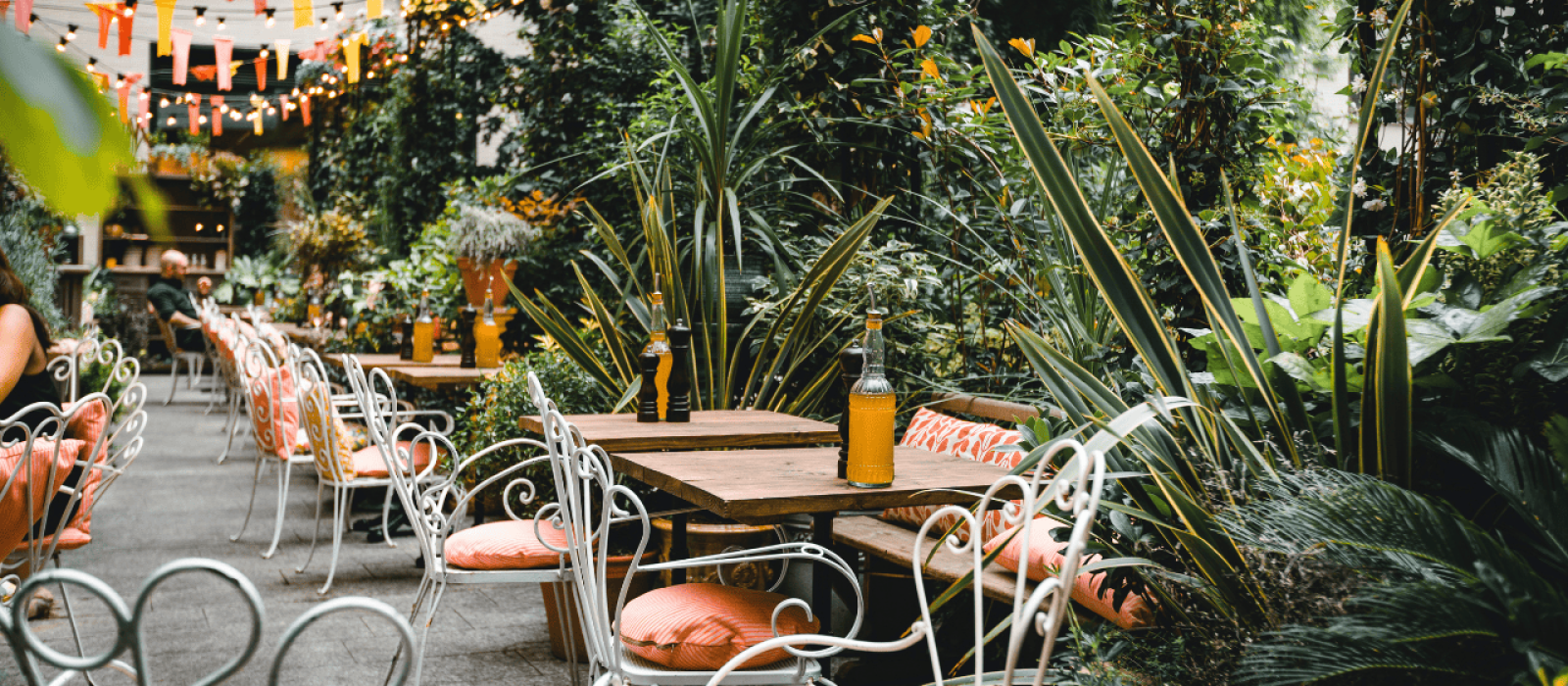 Gemütlicher Biergarten mit Holztischen, weißen Stühlen und üppiger Bepflanzung