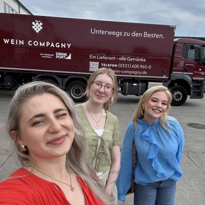 Drei Mitarbeiterinnen vor einem Wein-Company-LKW auf dem Betriebsgelände eines Getränkelogistikunternehmens