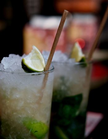 Erfrischender Cocktail mit Limettenscheibe, Crushed Ice und Holzstrohhalm in einem hohen Glas