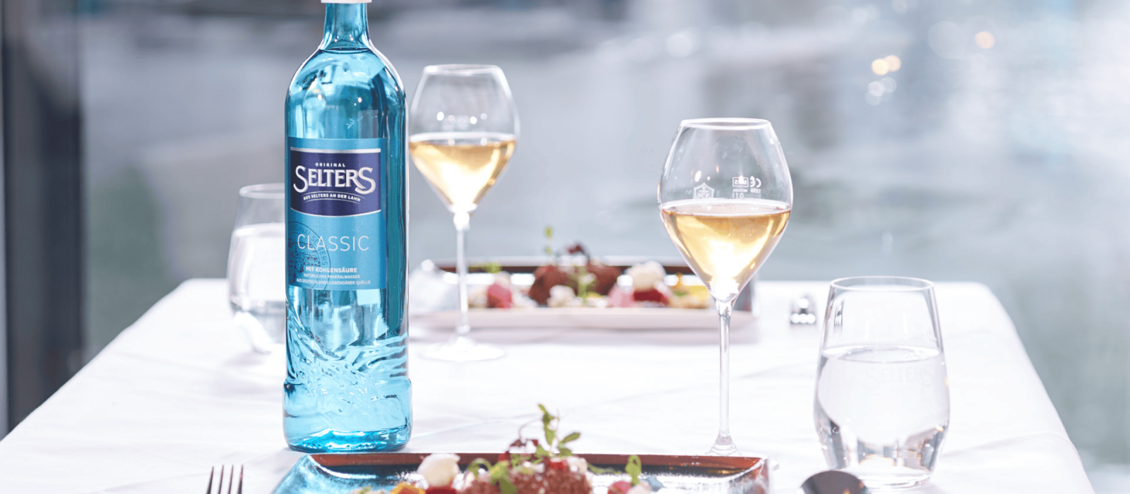 Selters Classic Mineralwasserflasche auf gedecktem Tisch mit Wein und Speisen